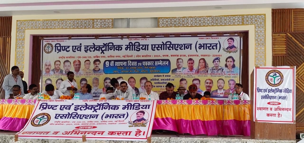 Panel of officials seated at a long table on a stage, with a large Hindi banner and portraits behind them, during a conference.