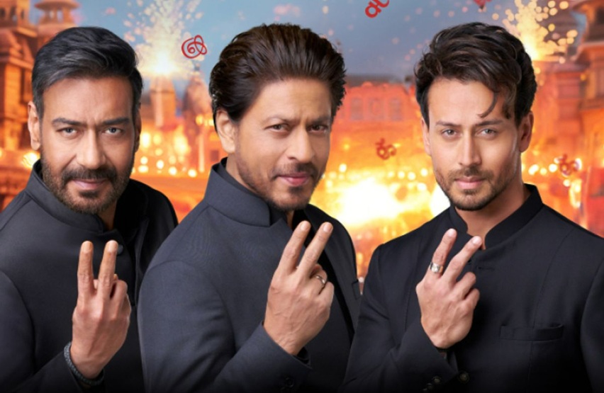 ajay_sharukh_tiger | No. 1 Indian Media News Portal Three men in dark suits pose with peace signs in front of a fireworks-filled festive backdrop.