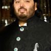 Portrait of a man in a black, ornate traditional outfit with green emerald-like buttons and a decorative chain.