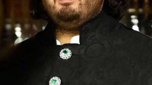 Portrait of a man in a black, ornate traditional outfit with green emerald-like buttons and a decorative chain.