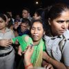 A woman in a green outfit is being escorted by uniformed officers through a crowded nighttime crowd.