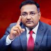 Professional man in a gray suit and red tie raises his index finger as if making a point against a red background.