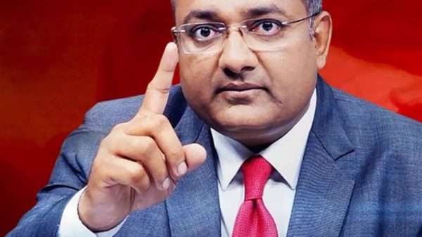 Professional man in a gray suit and red tie raises his index finger as if making a point against a red background.