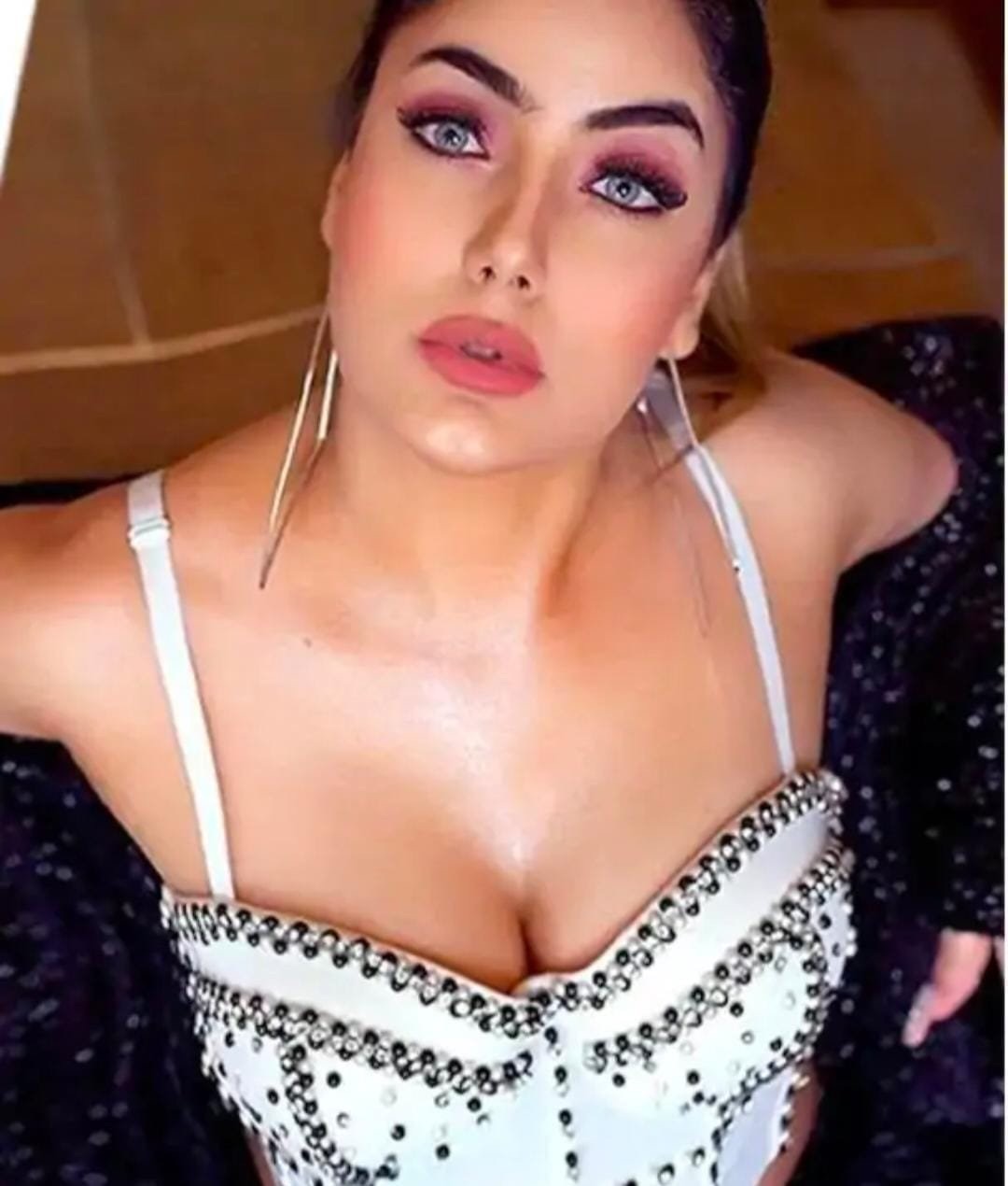 Woman wearing a white studded corset top and a dark sequined jacket, posing with bold makeup and smoky eyes.