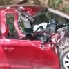 Red hatchback severely crushed in a crash, with a smashed front end and debris around it