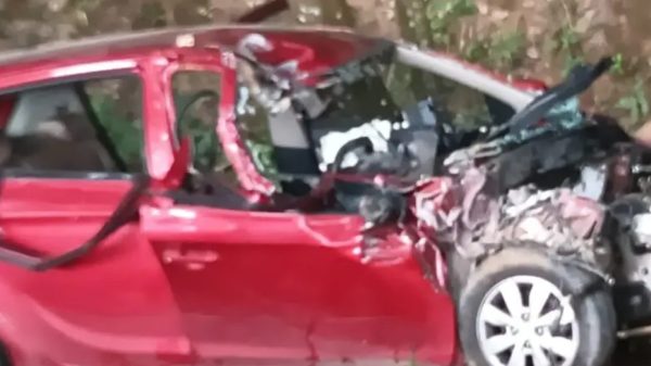 Red hatchback severely crushed in a crash, with a smashed front end and debris around it