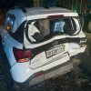 White SUV (Hyundai) with severe rear-end damage and luggage visible in the shattered hatch, at night by a truck on the road.