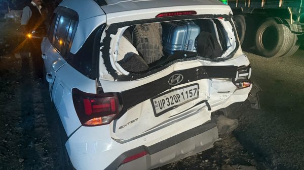 White SUV (Hyundai) with severe rear-end damage and luggage visible in the shattered hatch, at night by a truck on the road.