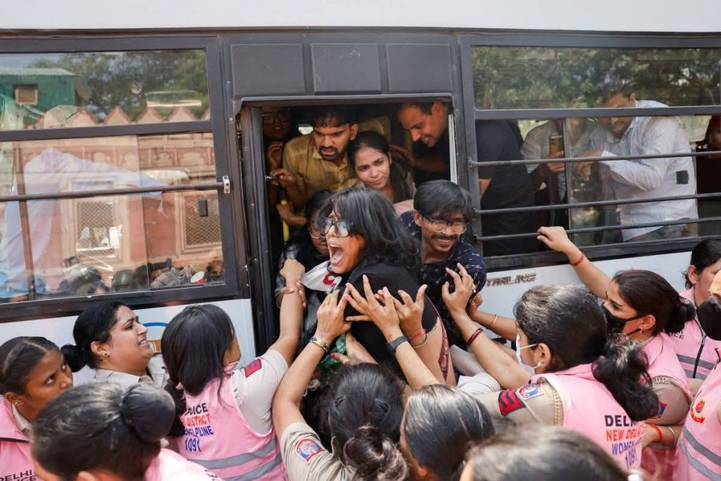 delhi protest_1 | No. 1 Indian Media News Portal Crowd of women in pink vests pull a woman out of a bus, expressions of urgency and help visible on a crowded street
