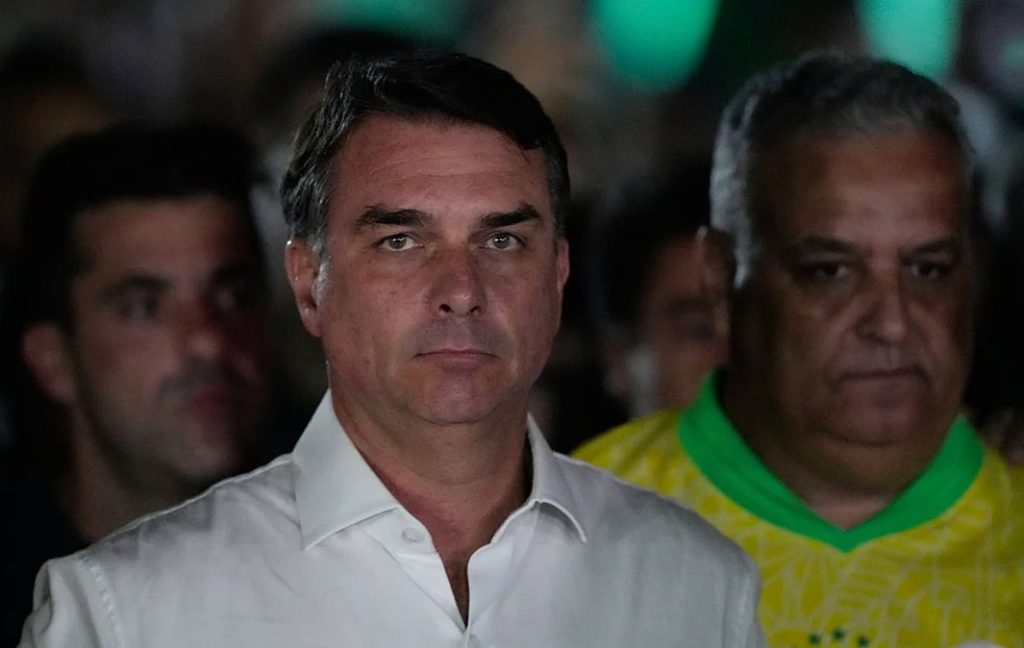 Man in a white button-down shirt with a serious expression at a crowded, dimly lit event.