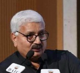 Man with white hair and glasses speaks into microphones at a podium.