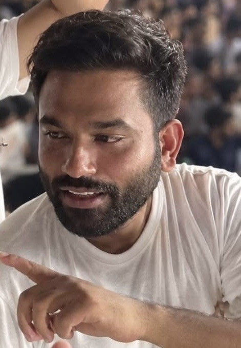Close-up of a bearded man in a white t-shirt, gesturing with his finger as he speaks.