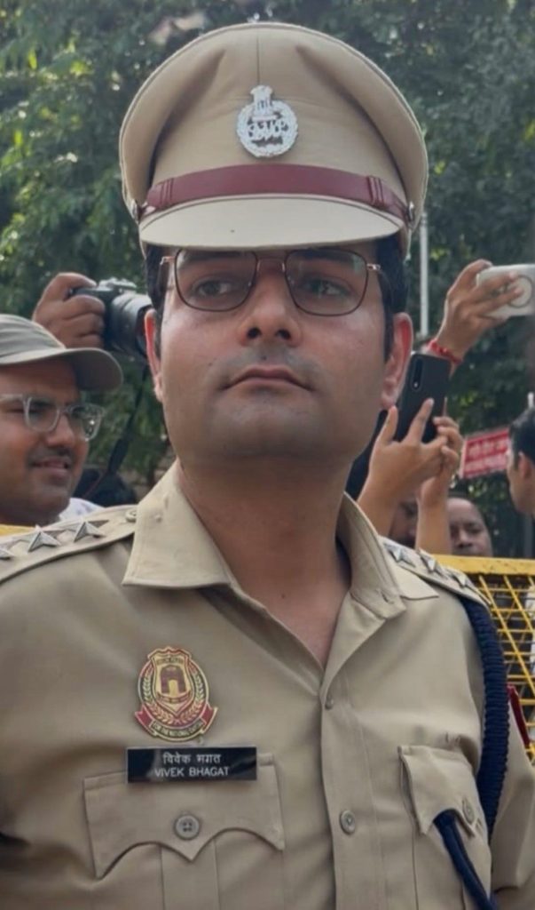 Close-up of an Indian police officer in khaki uniform, wearing a peaked cap; name tag reads Vivek Bhagat.