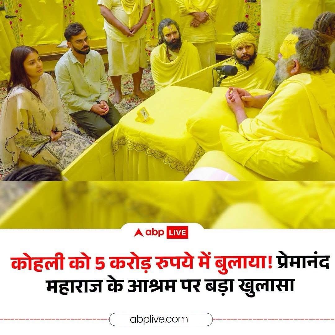 Group of people in yellow robes and light clothing sit and kneel around a yellow-clad speaker at a ceremonial or religious gathering, with a microphone on the table and a banner-like background behind them.