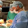 Surgeons in an operating room performing surgery with bright overhead lights and sterile gowns and masks.