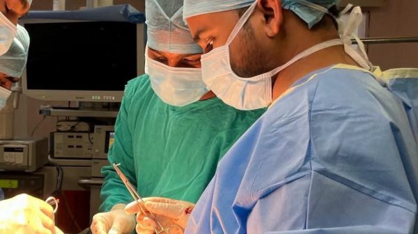 Surgeons in an operating room performing surgery with bright overhead lights and sterile gowns and masks.