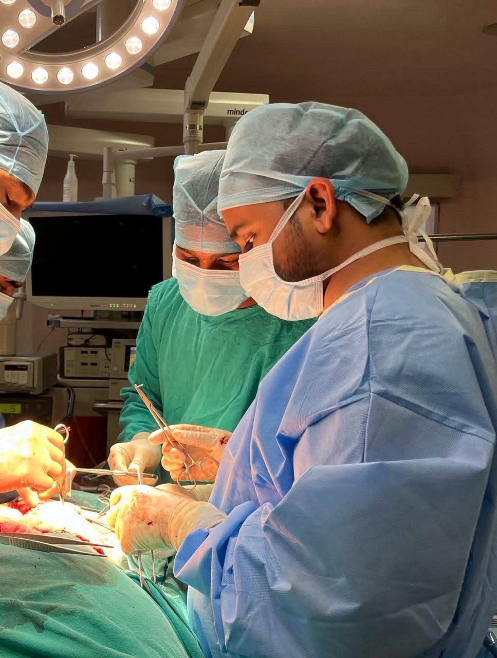 Surgeons in an operating room performing surgery with bright overhead lights and sterile gowns and masks.