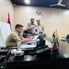 Police officers in khaki uniforms review documents at a conference table in an office room.
