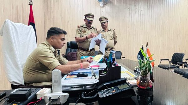 Police officers in khaki uniforms review documents at a conference table in an office room.