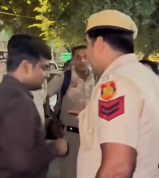 Screenshot | No. 1 Indian Media News Portal Police officer in a beige uniform and white cap speaks with a man on a city street at night, with bystanders in the background.