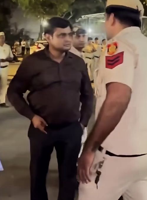 Screenshot | No. 1 Indian Media News Portal Man in a dark shirt chats with a white-uniformed police officer on a street at night, with a crowd in the background.