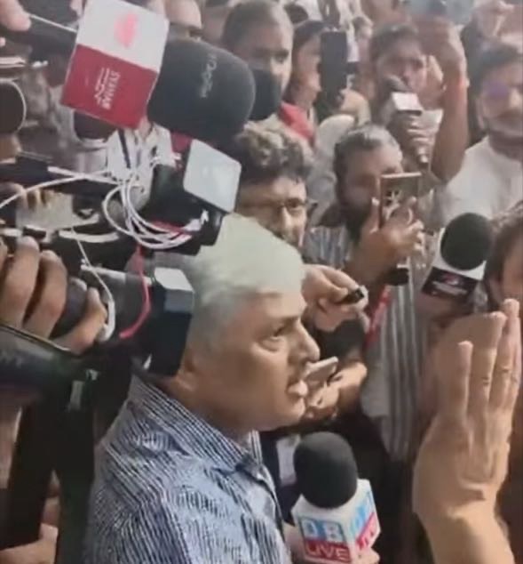 Screenshot | No. 1 Indian Media News Portal Man with white hair in a blue striped shirt speaks to a crowd of reporters; microphones, cameras, and people surround him as they record the moment.
