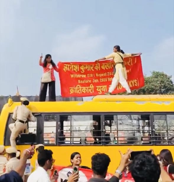 Screenshot | No. 1 Indian Media News Portal Police officers stand on a yellow bus as protesters raise a red banner on its roof, while a crowd watches nearby.