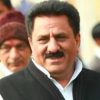 Close-up of a man with dark hair and mustache, wearing a white shirt and black vest, smiling at the camera.