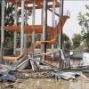 Construction site with bent orange stairwell and scattered metal sheets and debris after a collapse; solar panels lie on the ground.