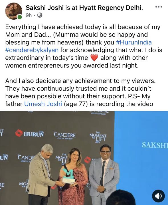 Screenshot | No. 1 Indian Media News Portal Three people on a stage at an awards ceremony; a woman in a red dress receives a trophy from a man in a beige suit, with another man beside them on the right.