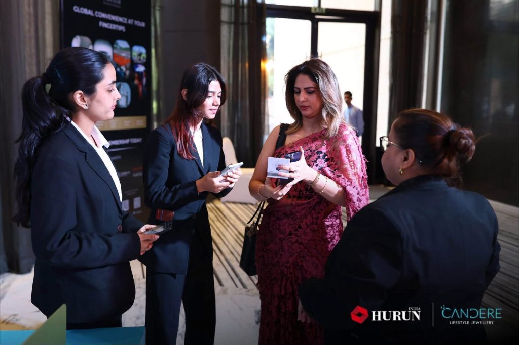 img_2398 | No. 1 Indian Media News Portal Group of four professionally dressed women in a lobby, one in a pink lace dress showing a card to two colleagues.