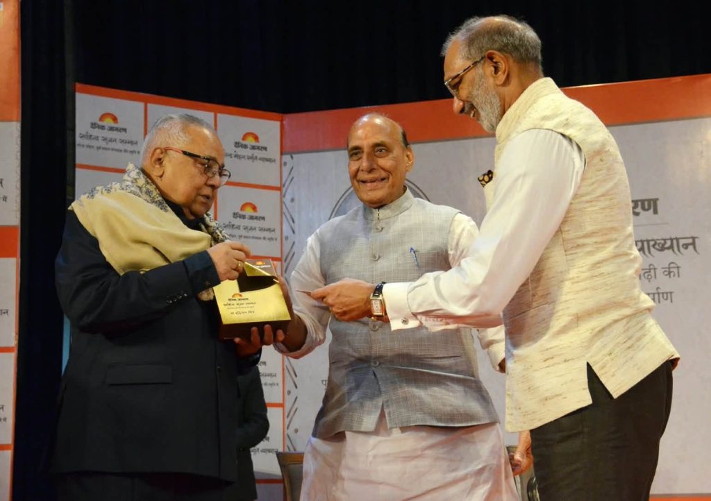jagran sahitya_1 | No. 1 Indian Media News Portal Stage award ceremony: a man in a light gray vest and white kurta receives a gold trophy from another man in a dark suit, with a third man smiling nearby.