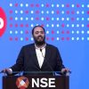 Speaker in a dark suit delivering a speech at a podium labeled NSE, with a Jio logo backdrop.