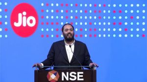 Speaker in a dark suit delivering a speech at a podium labeled NSE, with a Jio logo backdrop.