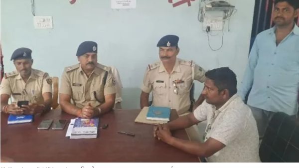 Police officers in khaki uniforms sit at a table with a civilian during a briefing about Katihar journalist kidnapping (captioned in Hindi).