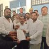 Group of men in a formal setting handing over a document or petition to a central man in white shirt; solemn event indoors.