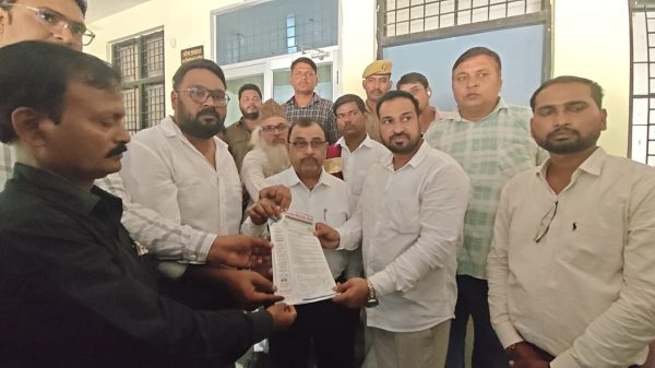 Group of men in a formal setting handing over a document or petition to a central man in white shirt; solemn event indoors.