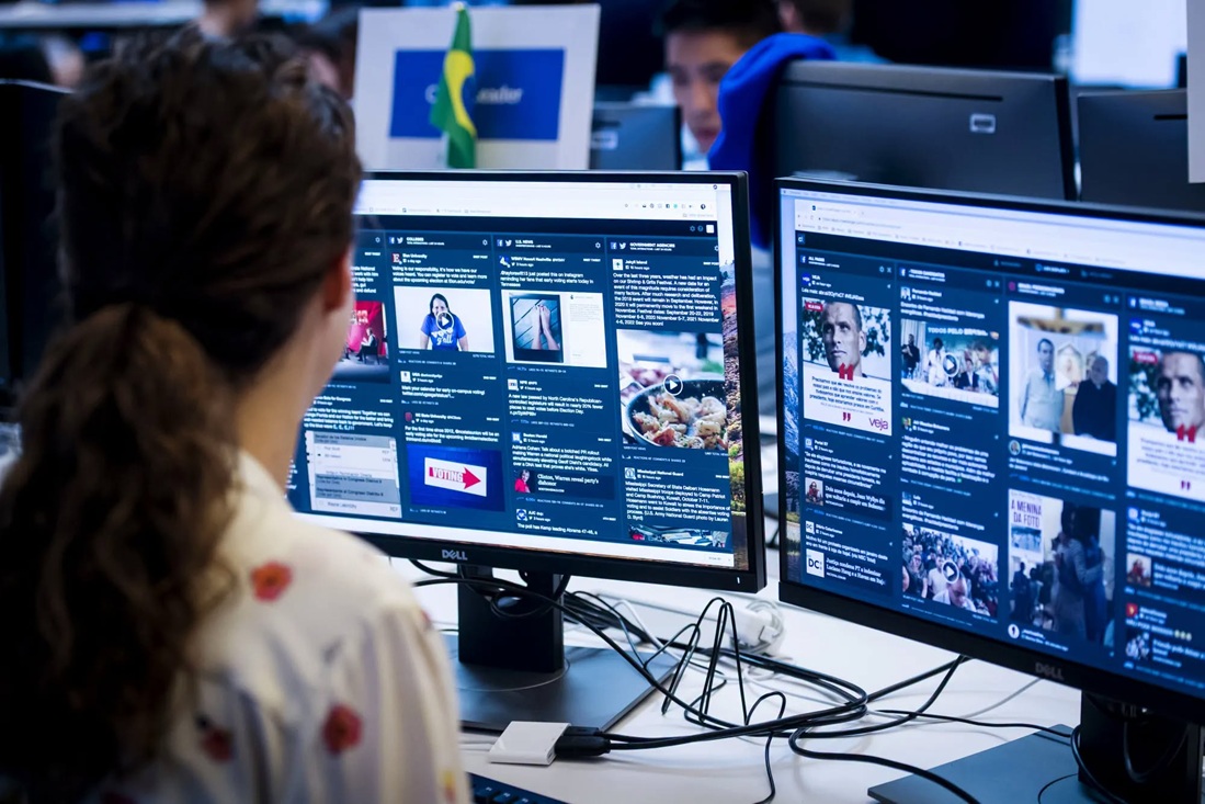lula_meta | No. 1 Indian Media News Portal Person seated at a desk viewing two large monitors filled with social feeds and news articles; a Brazilian flag is visible in the background.