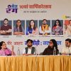 Panelists seated behind a long table with microphones and water bottles, in front of a large event banner featuring portraits and Hindi text.