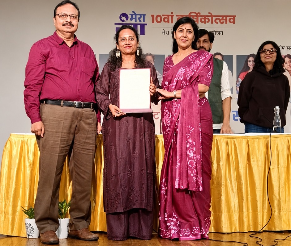 mera rang_1 | No. 1 Indian Media News Portal Award ceremony on a stage: man in maroon shirt and brown trousers alongside two women; the woman in purple holds a certificate as the other in a magenta saree presents it.