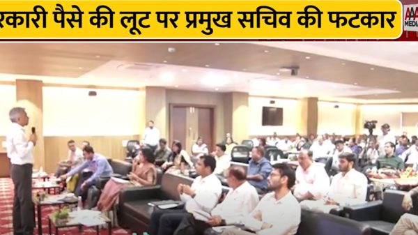 Speaker addressing a conference in a hall as attendees listen; a bold Hindi banner about government funds misuse is visible at the top.