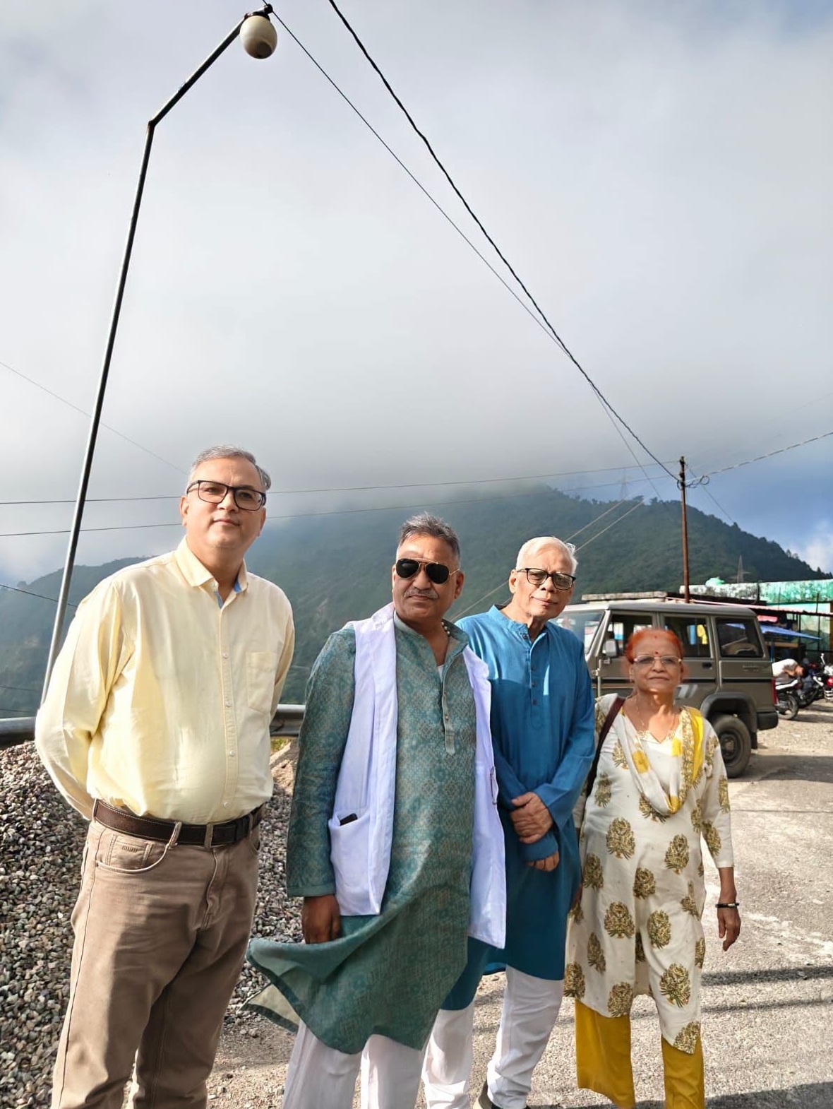 Four adults posing outdoors in a mountainous area, wearing traditional Indian clothing.