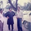 Four men stand together outdoors beside a white vintage car, with trees in the background.