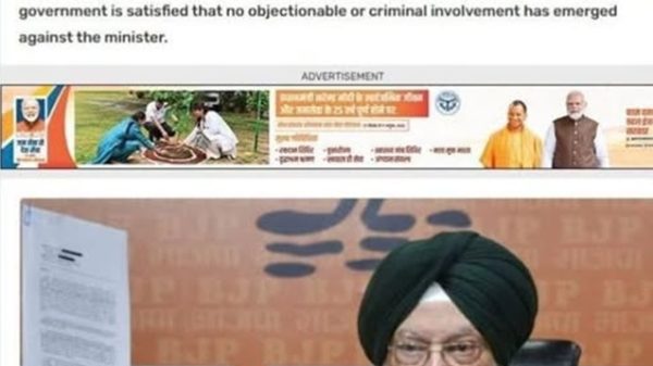 Man wearing a green turban and glasses holds up a document at a press conference.