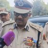 Police officer in tan uniform and cap speaks to reporters, sunglasses on, microphone held near him; text banner overhead reads: 'How Delhi Police Detained, Heckled, Tailled, And Questioned Quint Journalists Today'