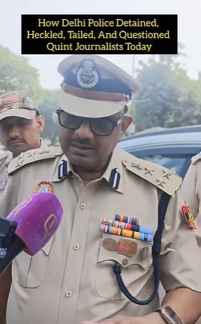 Police officer in tan uniform and cap speaks to reporters, sunglasses on, microphone held near him; text banner overhead reads: 'How Delhi Police Detained, Heckled, Tailled, And Questioned Quint Journalists Today'