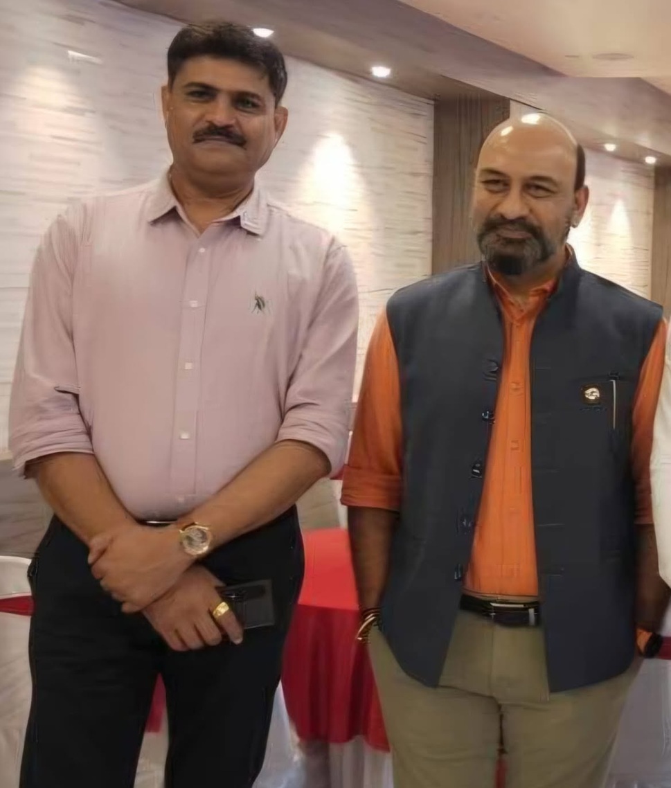 ravi mittal | No. 1 Indian Media News Portal Two men stand indoors side by side, posing for a photo: one in a light pink button-down shirt and black trousers, the other in an orange shirt with a dark vest and khaki pants.