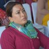 South Asian woman at an event, wearing a pink cardigan and green patterned scarf, with a red tilak on her forehead, looking to the side.