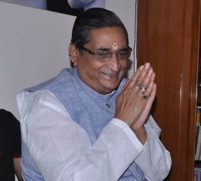 rk sinha_1 | No. 1 Indian Media News Portal Man wearing glasses and a light blue vest, hands pressed together in a namaste gesture, tilak on the forehead.