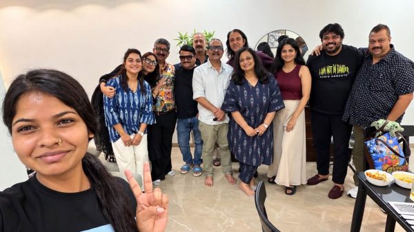 A group of friends posing together for a selfie indoors, smiling and standing in a casual party setting.
